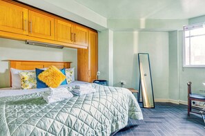 A neatly made bed with a quilted green blanket, wooden headboard, and decorative pillows. - Hardwood Home (London)