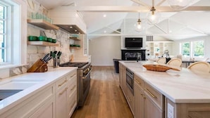 A modern kitchen with marble countertops, wooden cabinets, and a central island. - Elevate Your Cape Stay: Chatham Luxury with Pool & Beach RPAM026 (Chatham)