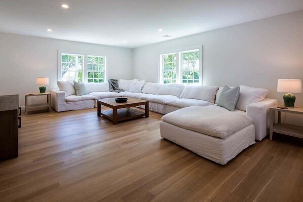 A modern living room with a sectional sofa, a coffee table, and two side tables. - Elevate Your Cape Stay: Chatham Luxury with Pool & Beach RPAM026 (Chatham)