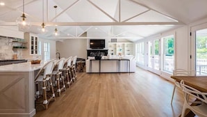 A spacious kitchen with a central island, white bar stools, and a dining table with chairs. - Elevate Your Cape Stay: Chatham Luxury with Pool & Beach RPAM026 (Chatham)