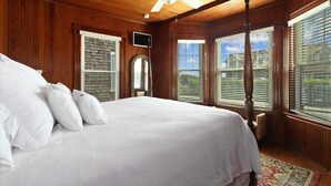 Een slaapkamer met een groot bed, houten wanden, een plafondventilator en uitzicht op buiten.