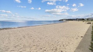Een breed zandstrand met een helderblauwe lucht en verspreide wolken.