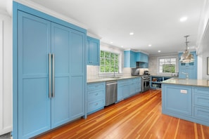 Una cocina con armarios azules, electrodomésticos de acero inoxidable y piso de madera.