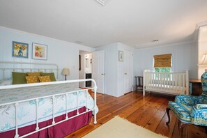 Un dormitorio con cama, cuna, silla y puerta que da a otra habitación.