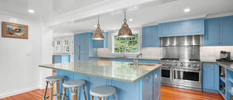 Una cocina moderna con gabinetes azules, una isla grande con taburetes, electrodomésticos de acero inoxidable e iluminación colgante.