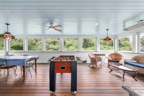 Une pièce lumineuse, avec une table de baby-foot, des meubles en osier et de grandes fenêtres.