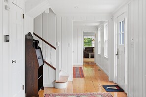A hallway with white walls, a wooden floor, and a staircase with a dark wooden handrail.
