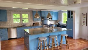 Une cuisine spacieuse avec des meubles bleus, un grand îlot central doté de tabourets, des appareils en acier inoxydable et un éclairage suspendu.