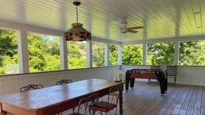 Une véranda couverte avec une table et des chaises en bois, un ventilateur de plafond et une table de baby-foot.