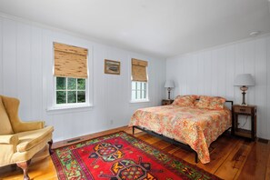 A bedroom with a bed, two bedside tables, a chair, and a window with a view of greenery.