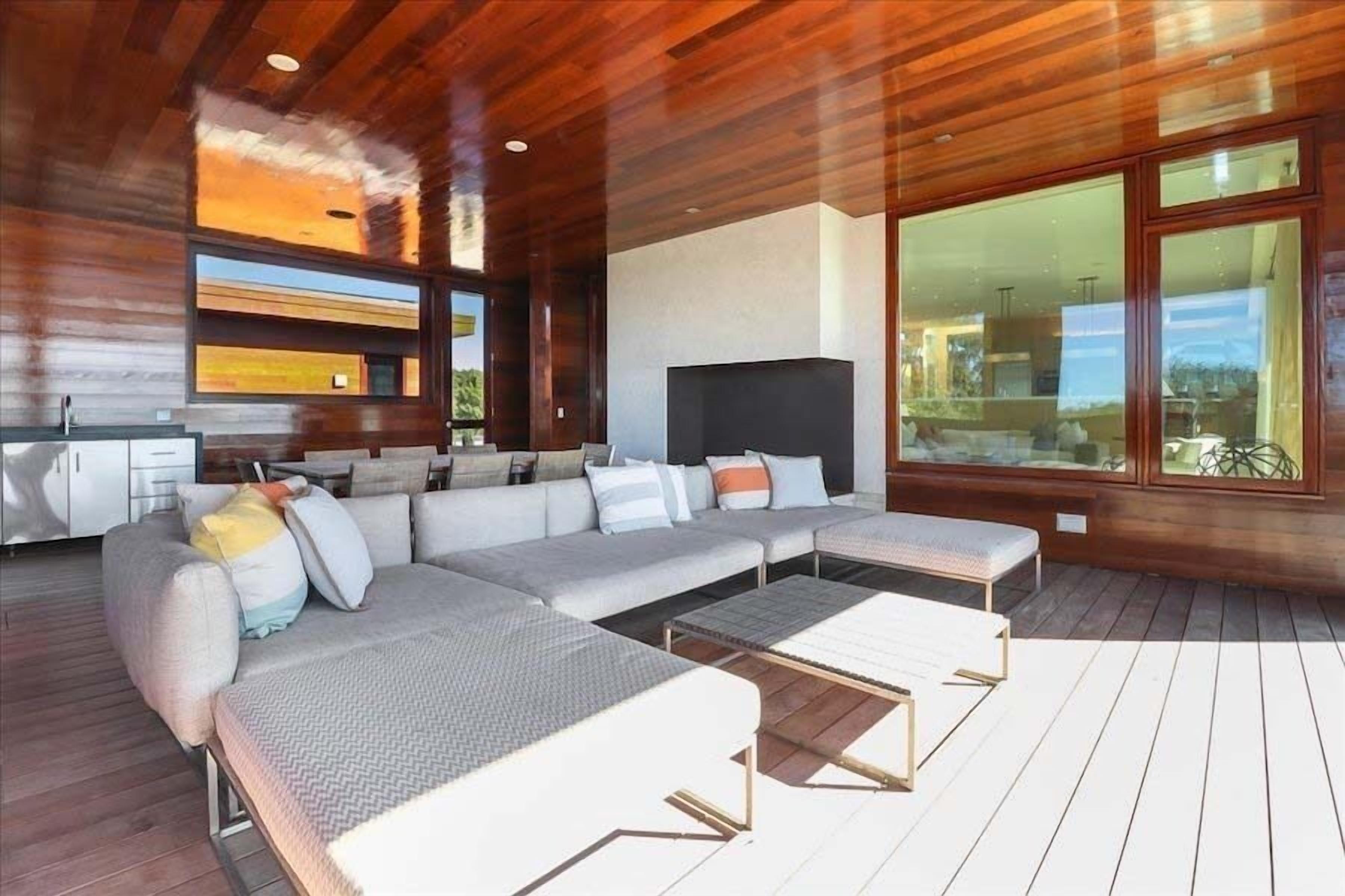 A modern living room with a large sectional sofa, a flat-screen TV, and a wooden deck.