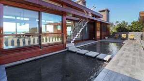Une maison moderne dotée d’une piscine, de grandes fenêtres et d’un escalier menant à une terrasse.