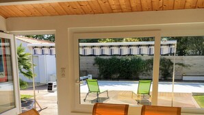 Un comedor con una mesa grande y cuatro sillas, techo de madera y vista a un patio con sillas y una valla.