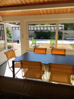 Ein Essbereich mit einem großen Tisch, vier Stühlen, einer Holzbalkendecke und Blick auf eine Terrasse mit Stühlen und einem Zaun.