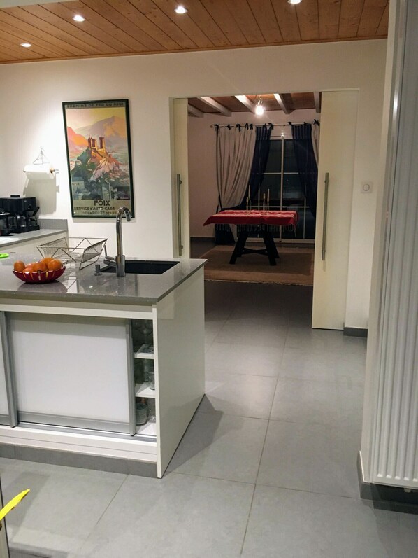Une cuisine moderne dotée d’un îlot central, d’un coin repas avec une table et des chaises, et donnant sur une salle à manger grâce à une fenêtre.