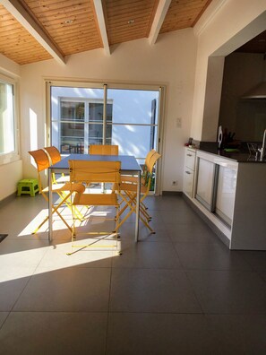 Une cuisine moderne avec un plafond en bois, un coin repas comprenant une table et des chaises, et une grande fenêtre qui laisse entrer la lumière naturelle.