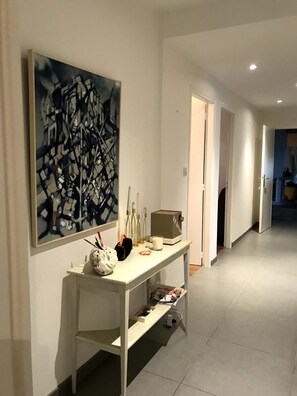 Un couloir avec une console blanche, un grand tableau abstrait et une porte donnant sur une autre pièce.
