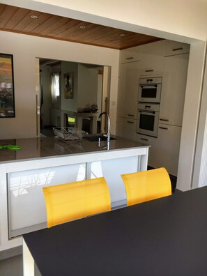 A modern kitchen with white cabinets, a black countertop, and a yellow chair.