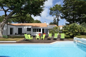 Ein Swimmingpool mit grünen Liegestühlen und ein Gebäude mit weißem Putz und einem gefliegelten Dach im Hintergrund.