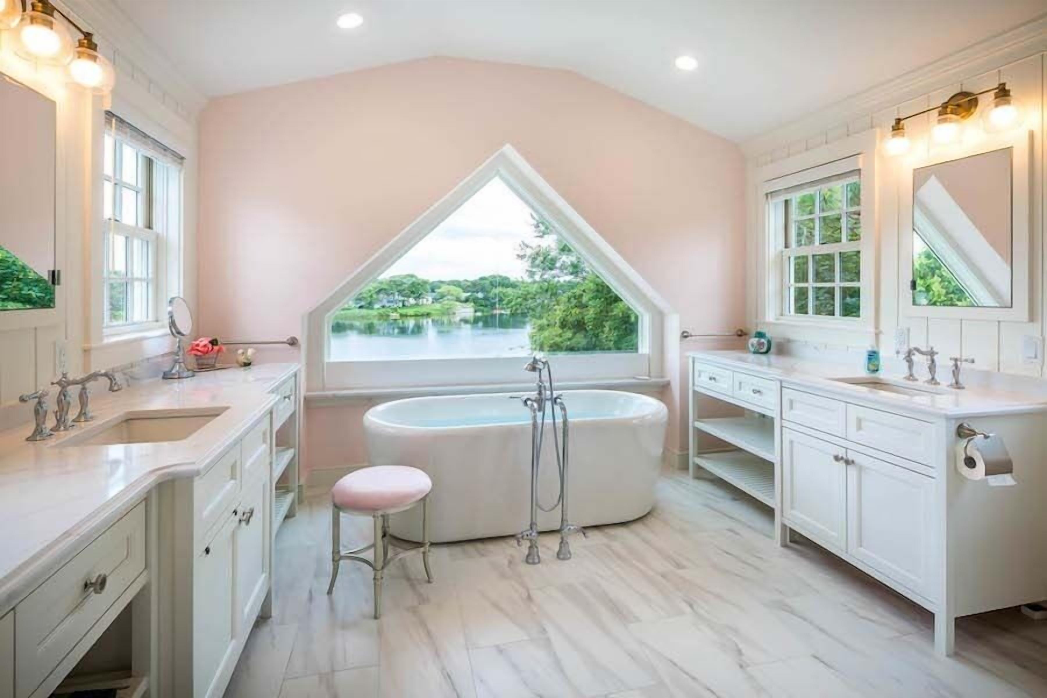 A bathroom with a freestanding bathtub, a vanity with a mirror, and a window with a view of greenery.