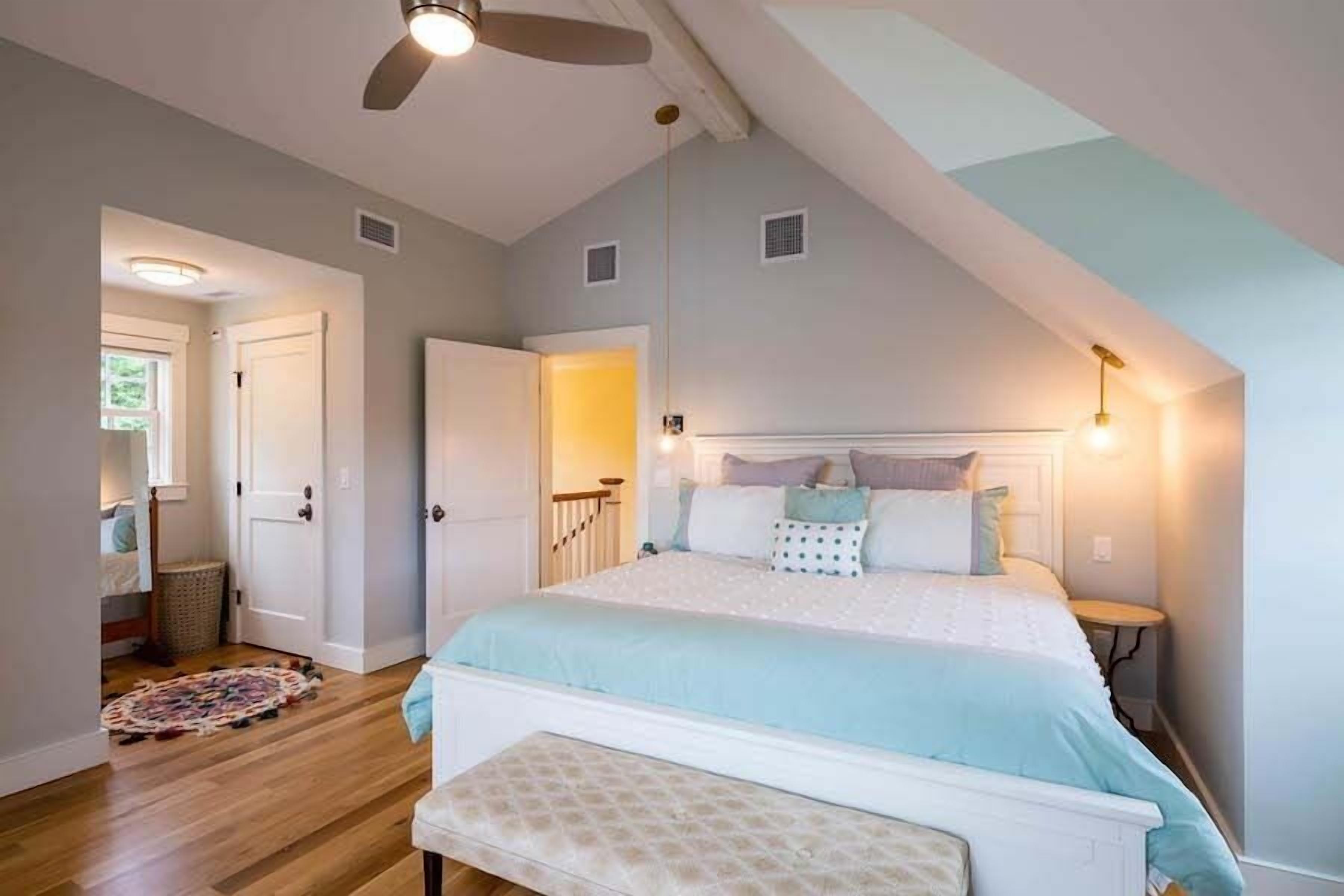 A bedroom with a large bed, a ceiling fan, a bedside table, and a nightstand.