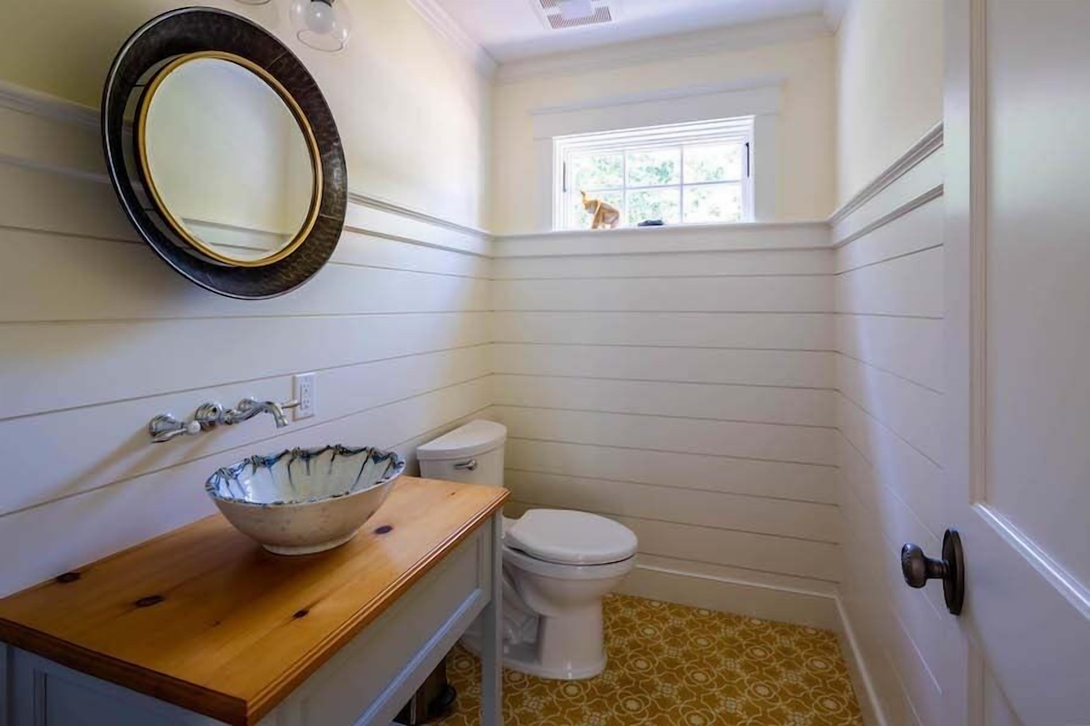 A bathroom with a wooden vanity, a white toilet, and a window with a view of greenery.