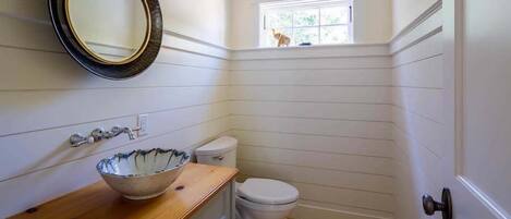 A bathroom with a wooden vanity, a white toilet, and a window with a view of greenery.