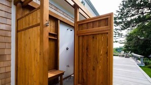 Un cerramiento exterior de madera para ducha con banco, puerta y una pequeña ventana.