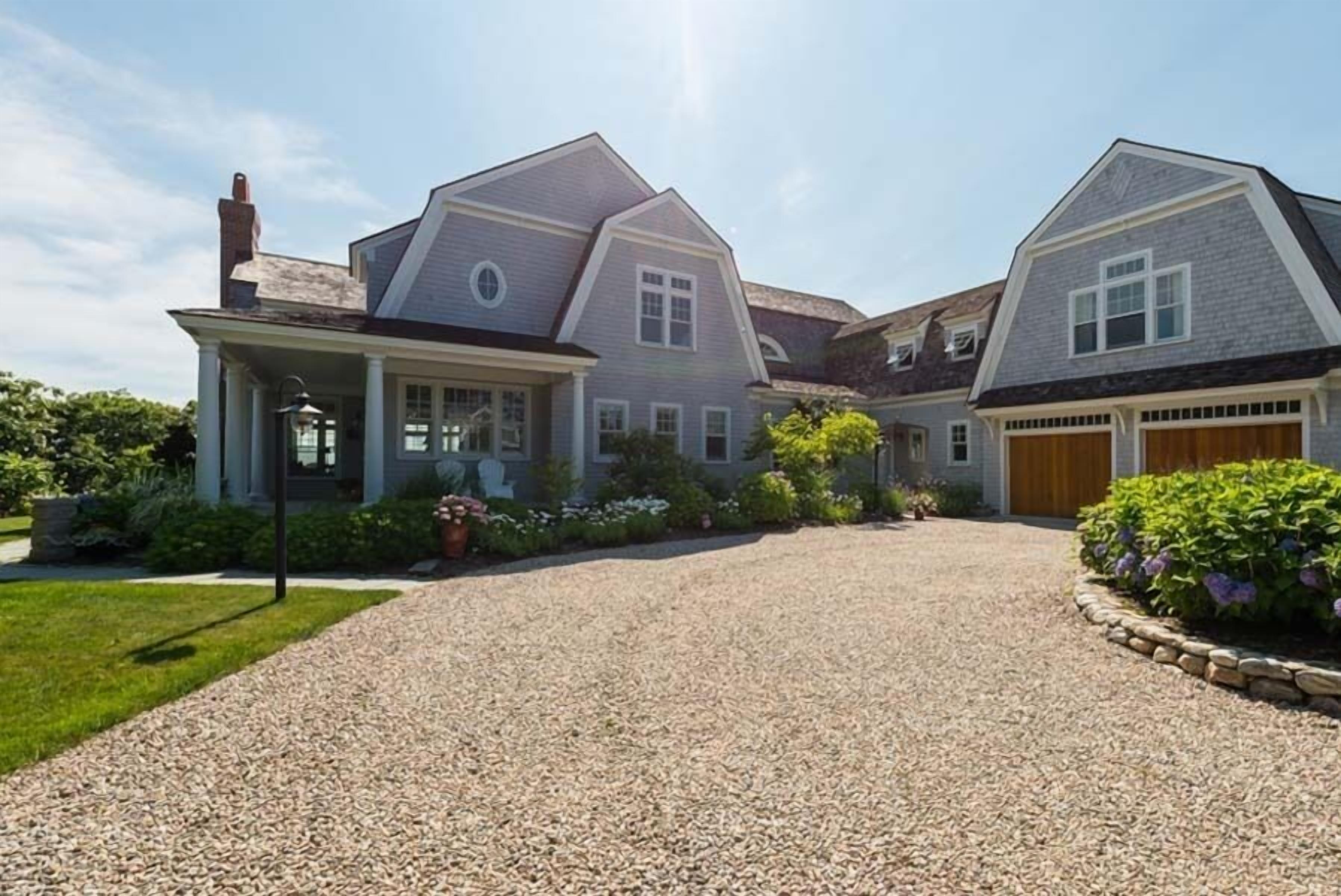 Ein großes, zweistöckiges Haus mit Schotterauffahrt, einer Veranda und einer Garage.