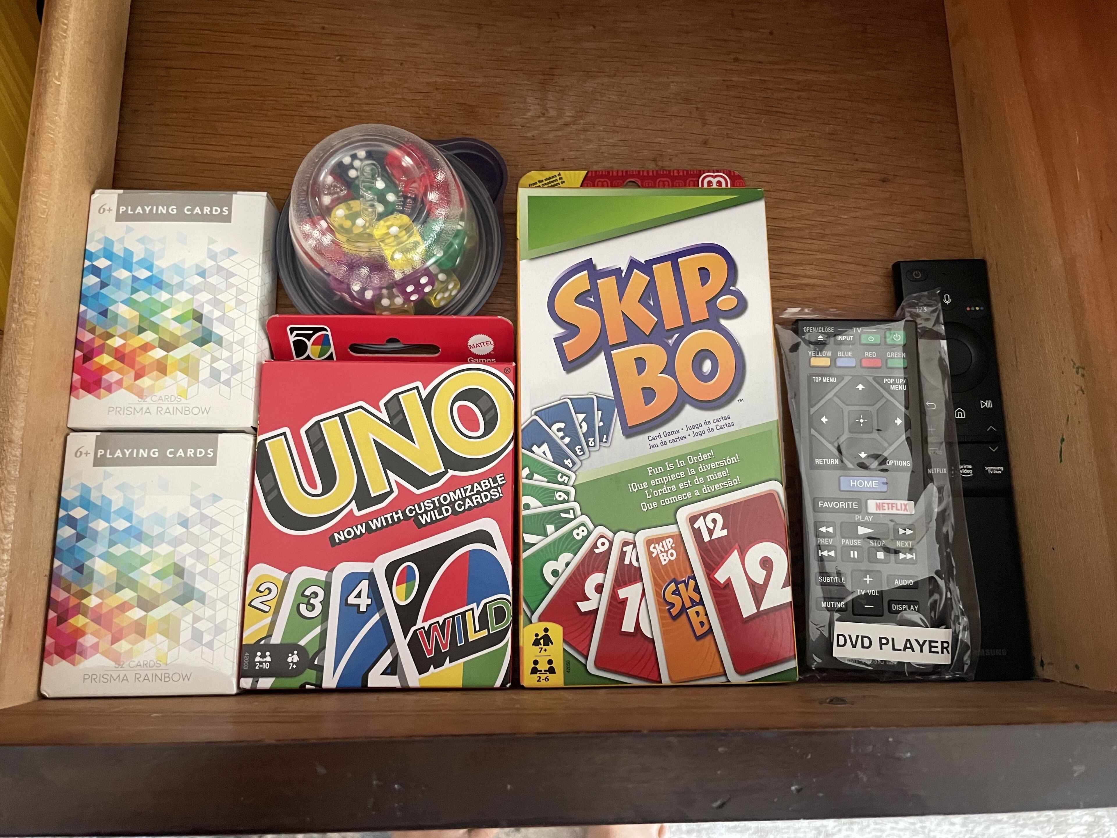 A drawer containing UNO cards, a DVD player, and a box of Prism Rainbow playing cards.