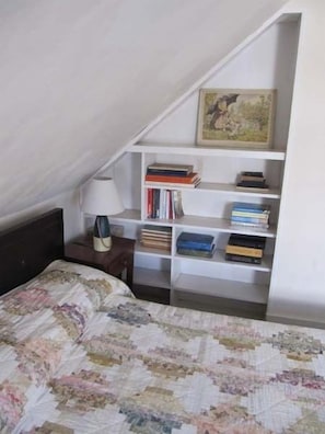 A bedroom with a bed, a bookshelf, and a painting.
