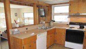 Una cocina compacta con armarios de madera, un lavavajillas blanco, una estufa y un lavamanos.