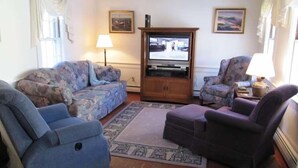 Una sala de estar con un sofá, sillones, un televisor y una lámpara.