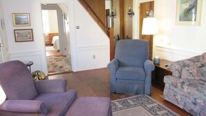 Una sala de estar con un sillón púrpura, un sillón azul, un sofá estampado con motivos florales y una alfombra con diseño.