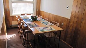 Un comedor con una mesa y sillas de madera, una ventana con persianas, y un interruptor de luz en la pared.