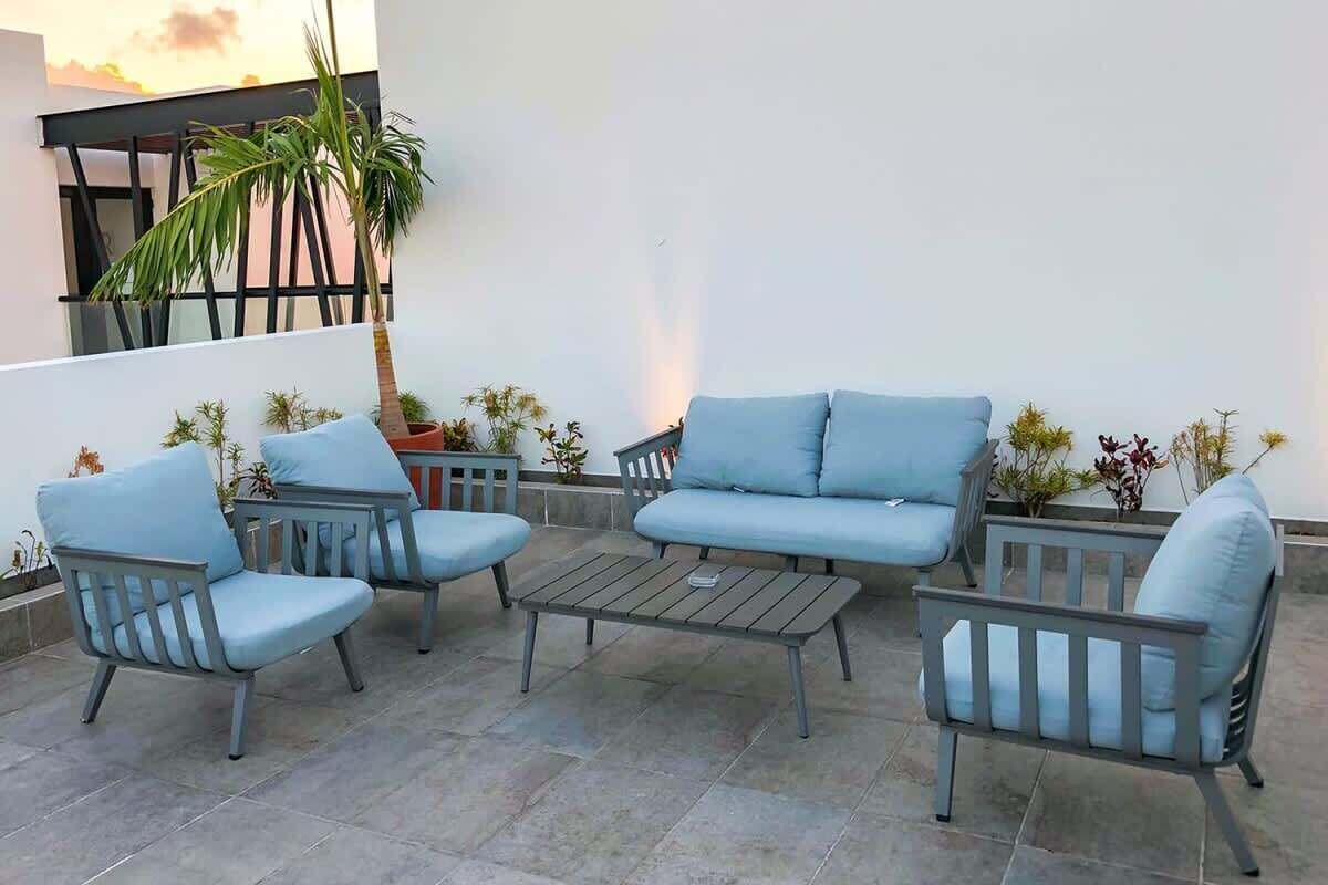 A patio with a blue sofa, two armchairs, and a coffee table. There are potted plants and a palm tree.
