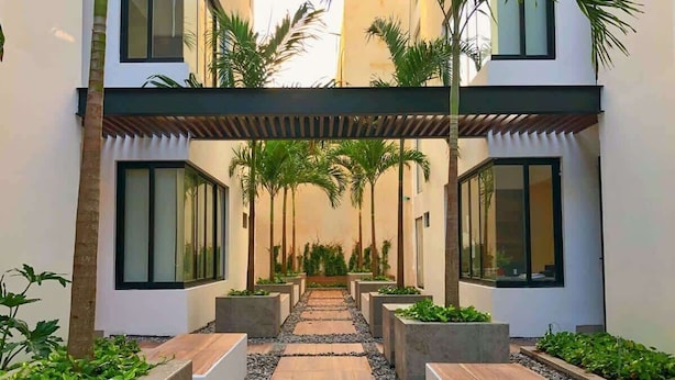 A modern building with a covered walkway, palm trees, and rectangular planters. - 5 Blocks to Beach | Icono Oceanview Pool & Hot Tub (Playa del Carmen)