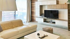 A modern living room with a sofa, a coffee table with decorative items, a flat-screen TV, and a window with curtains. - 5 Blocks to Beach | Icono Oceanview Pool & Hot Tub (Playa del Carmen)
