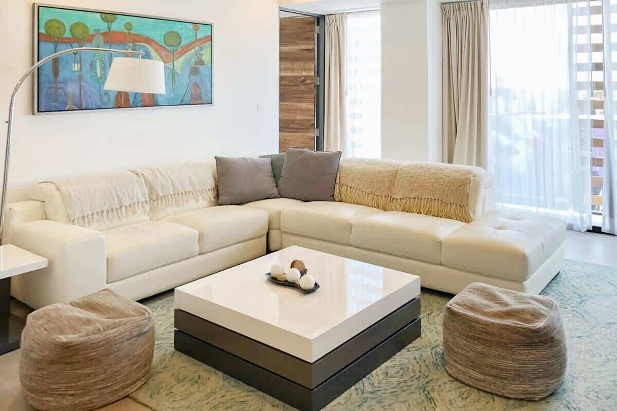 Una sala de estar moderna con un sofá blanco, una mesa de centro y dos otomanas.