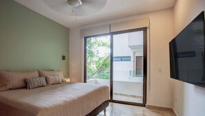 A bedroom with a bed, a TV, a sliding glass door to a balcony, and a ceiling fan. - Oceanview Rooftop Pool, Gym & 1 Block to 5th Ave (Playa del Carmen)