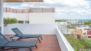 A balcony with two lounge chairs, a wooden deck, and a view of a coastal cityscape. - Oceanview Rooftop Pool, Gym & 1 Block to 5th Ave (Playa del Carmen)