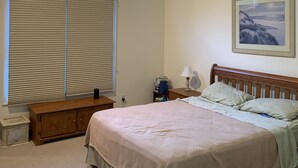 A bedroom with a large bed, a ceiling fan, a window with blinds, a bedside table with a lamp, and a framed picture on the wall. - Resort like Backyard-Pool, Putting green, Outside Kitchen, Fire Pit, Bar, Lounge (Hampton Bays)