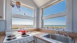 Une cuisine équipée d’une cuisinière, d’un évier et de grandes fenêtres donnant sur une plage.