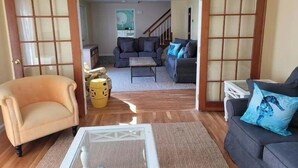A living room with a sofa, armchair, and coffee table, wooden flooring, and a view into the adjacent room through a doorway. - Newly renovated . Near sandy association beach RPMS090 (Dennis Port)