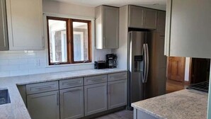 A modern kitchen with grey cabinets, a stainless steel refrigerator, and a window with wooden shutters. - Newly renovated . Near sandy association beach RPMS090 (Dennis Port)