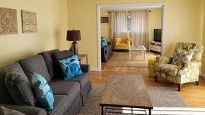 A living room with a sofa, armchair, coffee table, and a television in the background. - Newly renovated . Near sandy association beach RPMS090 (Dennis Port)