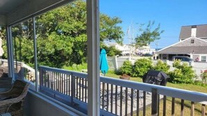 A covered outdoor area with a wooden deck, wicker chairs, and a view of a residential neighborhood. - Newly renovated . Near sandy association beach RPMS090 (Dennis Port)