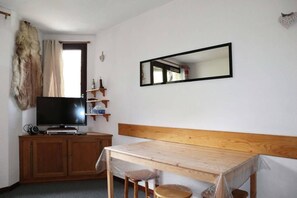 A room with a television on a wooden cabinet, a mirror on the wall, and a table with chairs. - 50m from ski slopes, 3rd floor, balcony, 26m², Les Orres (Les Orres)