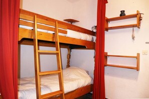 Un lit superposé avec une échelle, une étagère au-dessus et une étagère fixée au mur, sur laquelle se trouve un vase.