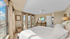 Un dormitorio con cama, televisor, ventilador de techo y vistas al exterior.